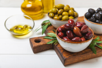 Green and black olives on a textured background. Different types of olives in bowls and olive oil with fresh olive leaves. Delicacy.Mediterranean Kitchen. Copy space.