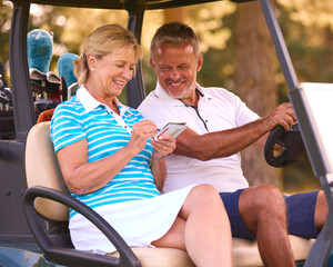 Senior Couple Sitting In Buggy On Golf Course Marking Score Card Together