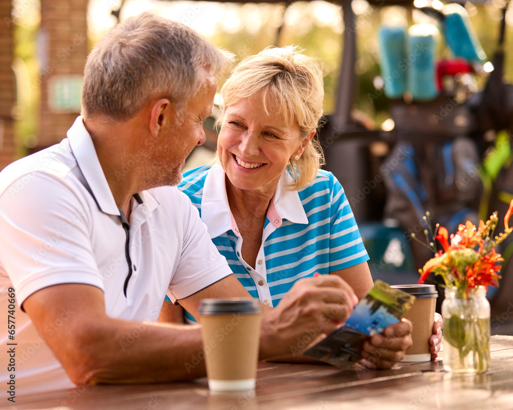 Wall mural Senior Couple Sitting Having Coffee After Round Of Golf Looking At Score Card Together