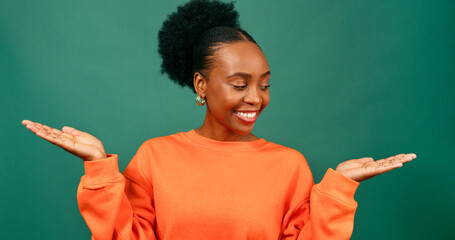 Beautiful young Black woman holds palms up weighing up choice, green studio