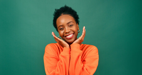 Beautiful Black woman cups hands under chin in cute pose, green studio