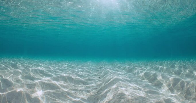 Transparent turquoise ocean with sandy sea bottom and sunlight in Bahamas. Underwater view