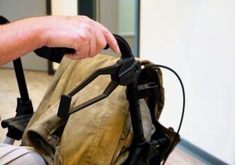 Hand von alter sitzender Frau hält schwarzen Griff von Gehwagen in Wartebereich in Arztpraxis 