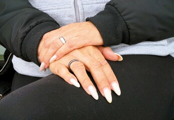 Übereinander geschlagene Hände mit langen weißen Fingernägeln auf Oberschenkel von sitzender...