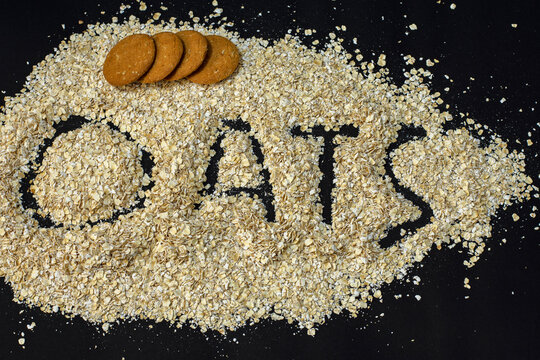 Homemade oatmeal cookies places on oats flakes with oats written on black background, top view, close up. Healthy food. Oatmeat biscuits recipe.
