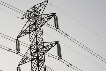 High-voltage electricity pylon supporting power lines with insulators against a cloudy sky,...