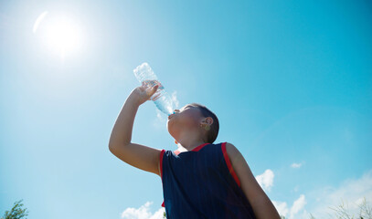 Little asian boy drinking water against blue sky