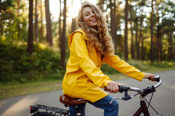 Smiling woman on a bicycle in an autumn park. Beautiful female tourist rides a bicycle, enjoys the sunny warm weather. Lifestyle, weekend concept. 