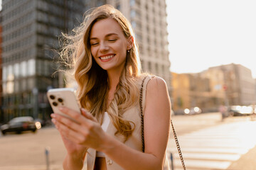 woman walking in sunny city street with phone
