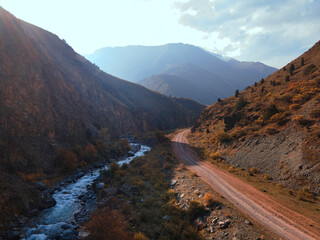 Mountain autumn landscape. dirt road with a stream and forest in toned colors in Kyrgyzstan