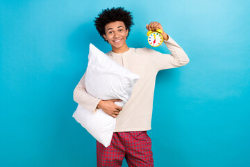 Photo portrait of nice young guy hold pillow clock timer wake up wear trendy white pajama outfit isolated on blue color background
