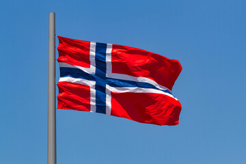 Norwegian flag waving in the wind against blue sky.