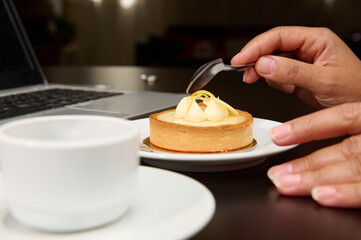 Close-up female hand holding a tea spoon over a French dessert with lemon custard, enjoying her...