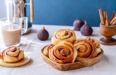 Homemade fresh baked cinnamon rolls in a wooden tray, cinnamon sticks, fig, coffee-pot and cappuccino 