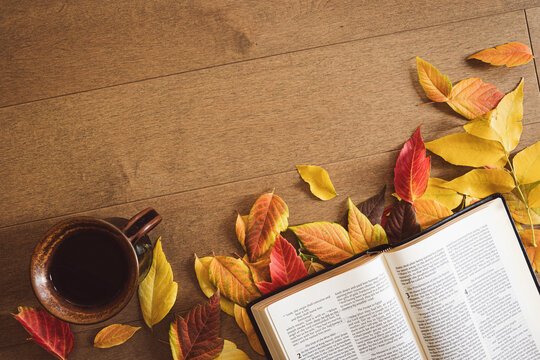 Christian bible and coffee with a border of autumn leaves on a light wood table with copy space