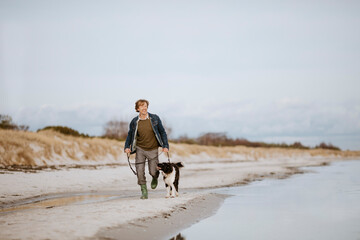 Wide angle view of a middle aged man running with his dog on the beach