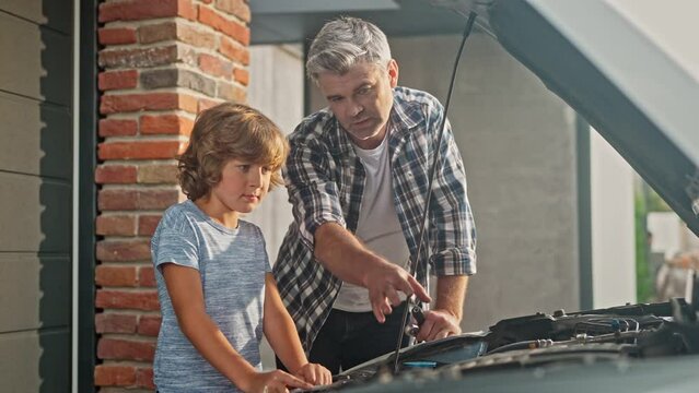Little Caucasian child helping his loving father diagnosing broken car. Attractive dad showing his son mechanism of working engine. Young boy helping repairing family auto. Concept of happy childhood.