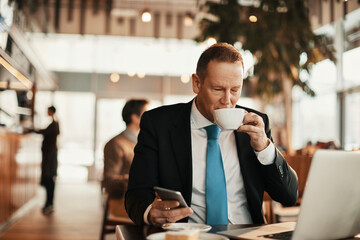 Middle aged businessman using a laptop and drinking coffee in a cafe decorated for christmas and the new year holidays