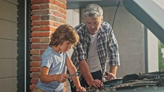Caucasian dad teaching his cute son working with mechanical tools during repairing their car. People looking on engine and searching for damage location. Happy father enjoying working with his child.