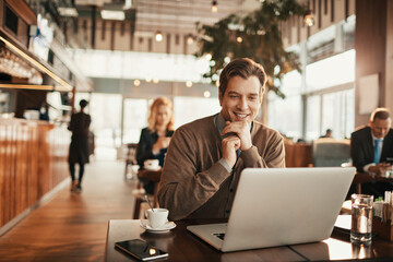 Young businessman using a laptop in a cafe decorated for Christmas and the new year holidays