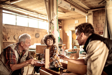 Multigenerational family of male carpenters teaching their youngest one the ways in a carpentry shop