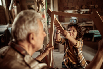 Senior male carpenter showing his grandson a wood frame in a carpentry shop