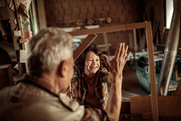 Senior male carpenter showing his grandson a wood frame in a carpentry shop