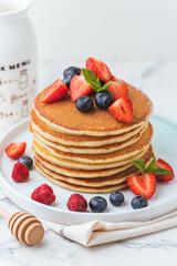 Stack of fresh pancakes with strawberries and blueberries drizzled with maple syrup and honey. Healthy traditional American breakfast on the white background