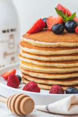 Stack of fresh pancakes with strawberries and blueberries drizzled with maple syrup and honey. Healthy traditional American breakfast on the white background