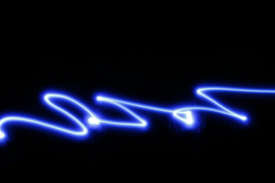 Los garabatos de luz de neón azul, en velocidad y desenfoque con diferentes formas de viboreo, forman un diseño abstracto en el espacio con fondo negro