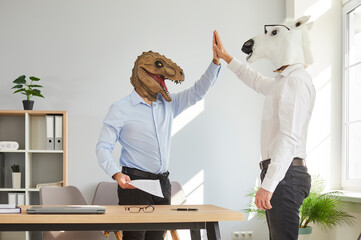 Two businessmen in animal masks giving high five celebrating achievement in office. Office workers,...