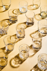 Various empty whiskey glasses on golden background with shadows.