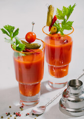 Glasses of bloody mary cocktail with shaker and spoon on light kitchen board