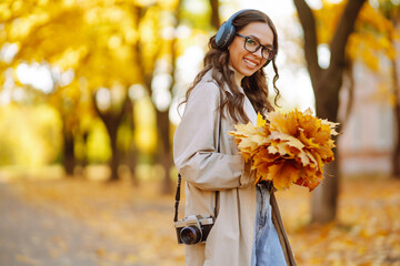 Happy young woman in stylish clothes takes pictures with a retro camera, having fun and relaxing in the autumn sunny park. The concept of relaxation, leisure activities.