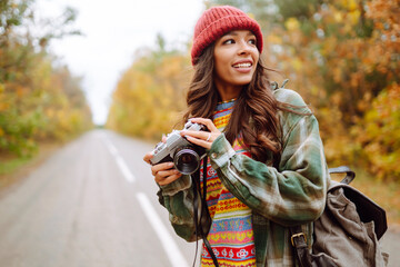 Woman tourist with a retro camera and backpack on a hike in a yellow autumn forest. Young woman walking and having fun outdoors.