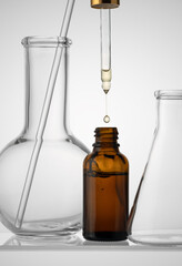 Bottle with liquid serum and dropper on a white background top view. Serum drops from a pipette.