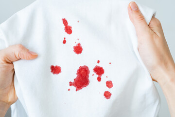 Female hands showing dirty blood stain on white cloth. Spoiled clothes. Dirty stain for cleaning...