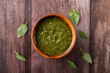 Pesto sauce on wooden bowl. Rustic background. Basil leafs on wooden background.