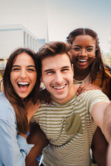 Vertical portrait of a happy multicultural friends laughing taking a selfie together. Mixed teenage...