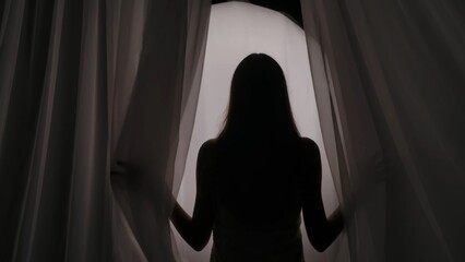 Medium shot of a young woman's silhouette wrapped in a towel coming from behind the curtain, on a...