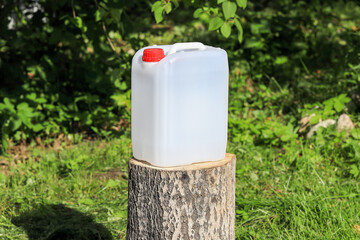 White plastic water canister stands on a stump in the garden