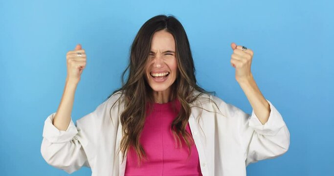 Amazed excited woman hairstyle in white shirt, pink top open mouth in surprise looking at camera with big eyes, shocked. Indoor studio shot isolated on blue background. Oh my god wow, yes gesture.