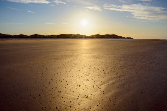 Sun reflecting on the sandy beach at low tide with the North Sea at sunrise at Bamburgh in Northumberland, England, United Kingdom
