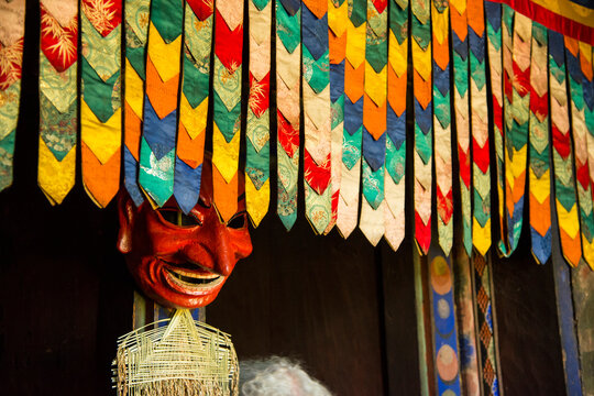 Mask displayed in a farmhouse behind hanging colorful decorative fabric; Paro Valley, Bhutan