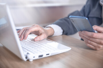Woman typing on laptop while holding phone
