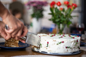 Close-up of a cake decorated with white cream with pomegranate seeds and rosemary. Female hands...