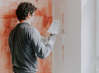 A Caucasian young man is putting putty on the wall.