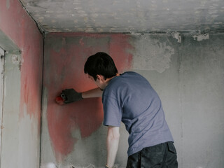 A young handsome caucasian builder applies a red hardening mortar to the wall with a large brush