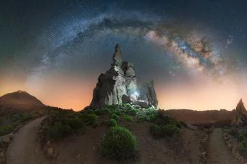 Foto op Plexiglas Canarische Eilanden The arch of the Milky Way illuminates Los Roques de Garcia. A man with a lantern next to a gorgeous rock formation at Teide National Park in Tenerife, Canary Islands, Spain