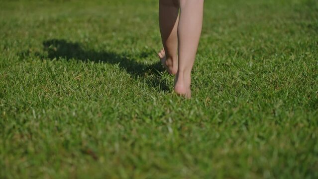 Small child walking barefoot shadow on grass Closeup super slow motion
